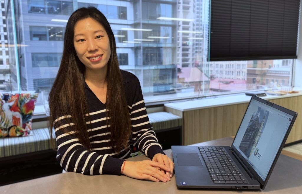 Grace smiling in the ADF office break out area in front of her laptop